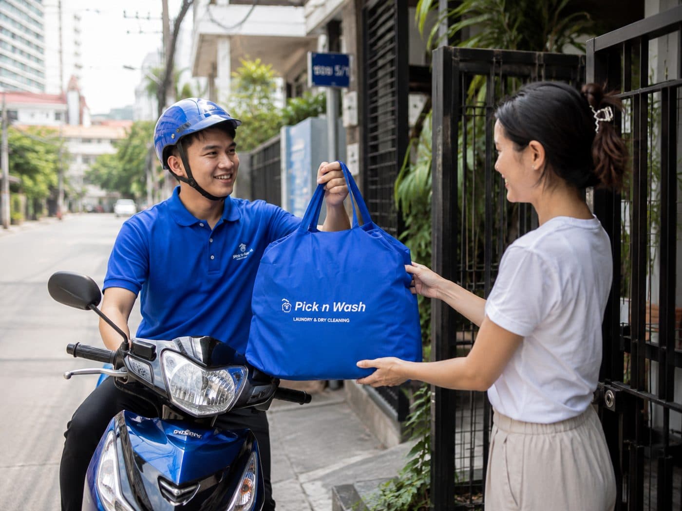 พนักงาน Pick n Wash ในเครื่องแบบ ส่งถุงผ้า Pick n Wash ให้ลูกค้าที่หน้าบ้าน